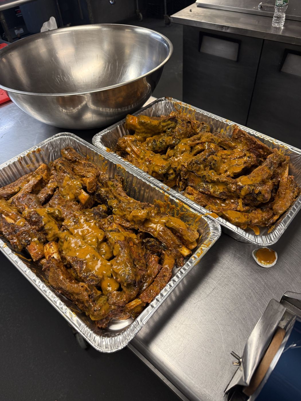 Two full pans of sauced beef ribs in a commercial kitchen